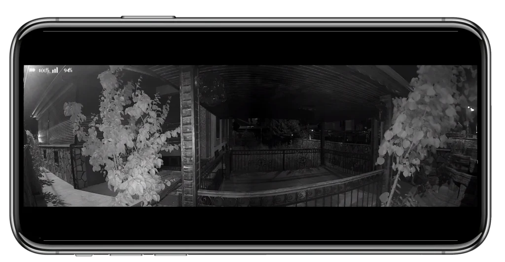 Nighttime security camera view of a covered porch area with plants on both sides and a metal railing, displayed on a smartphone screen.